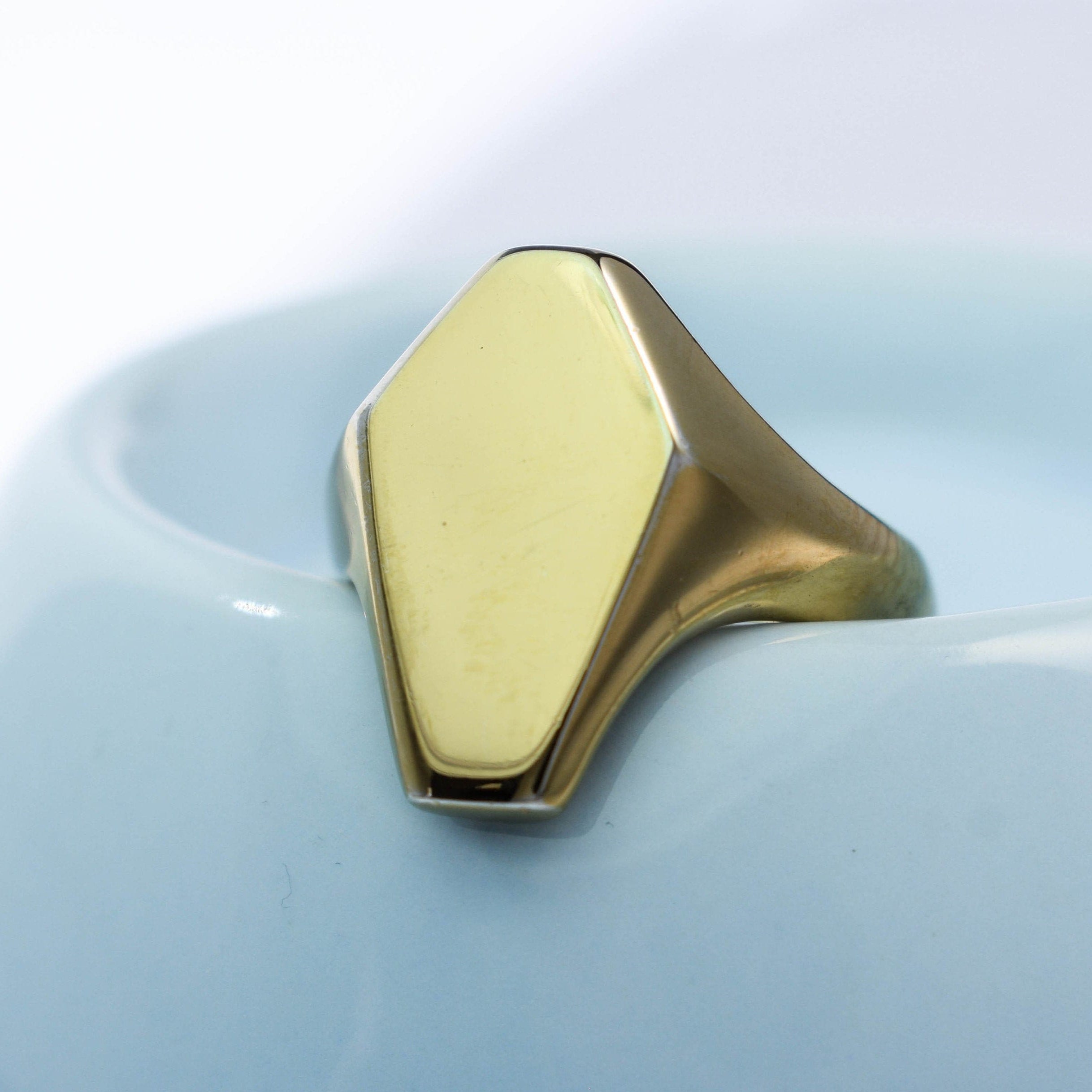 A gold-colored coffin-shaped signet ring placed on a light blue surface.