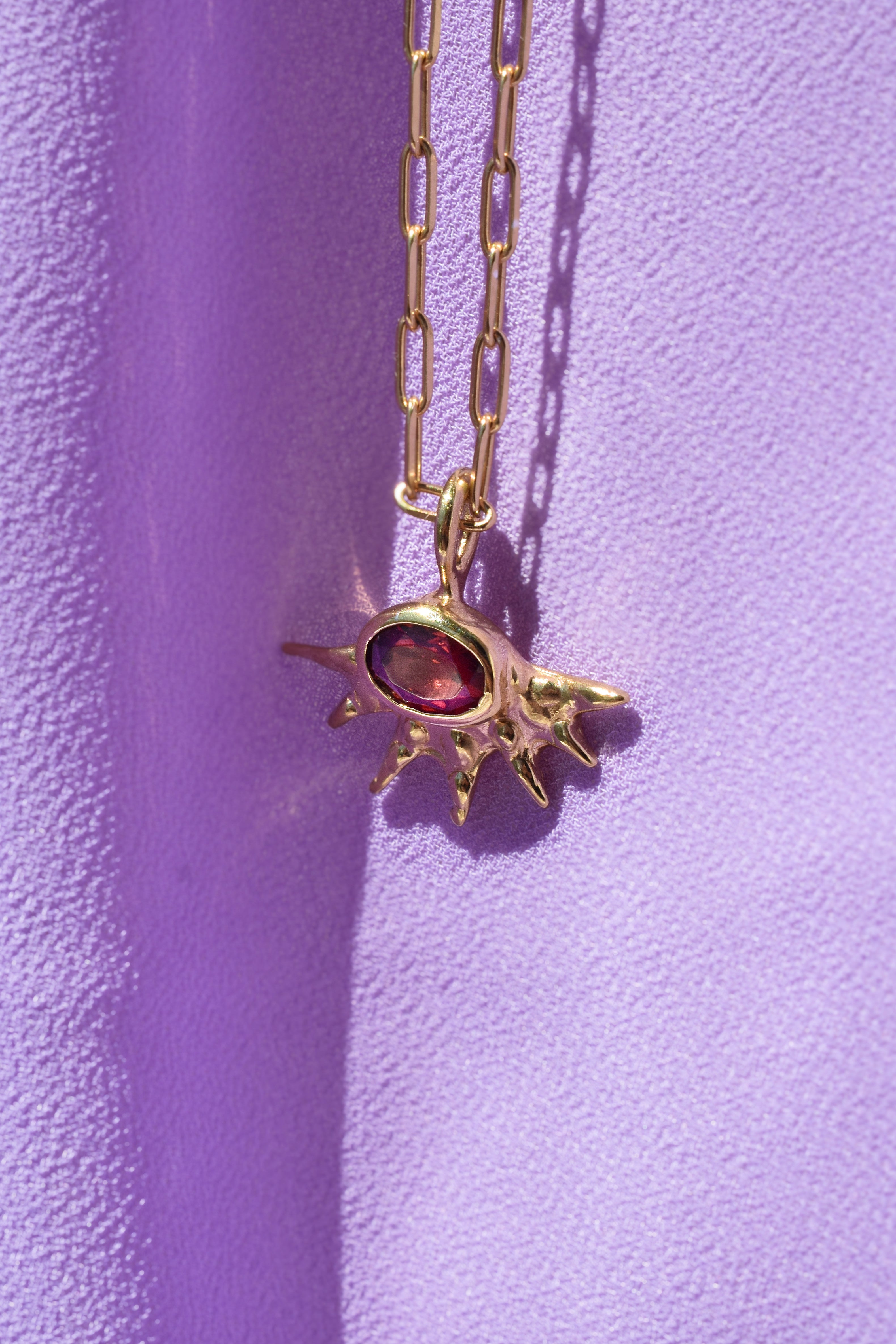 A radiant pendant on a paperclip chain, featuring a deep red garnet at the center of an asymmetrical, spiked gold setting. Bold and edgier than a traditional sunburst, it's easy to wear solo or layered.