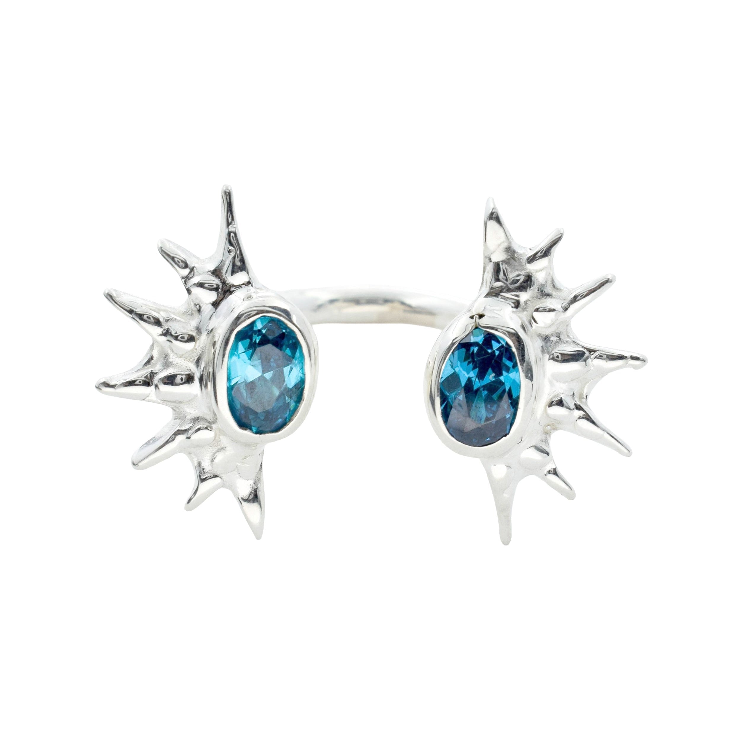 A silver-toned spiky cuff ring featuring two oval blue gemstones, set against a plain white background.