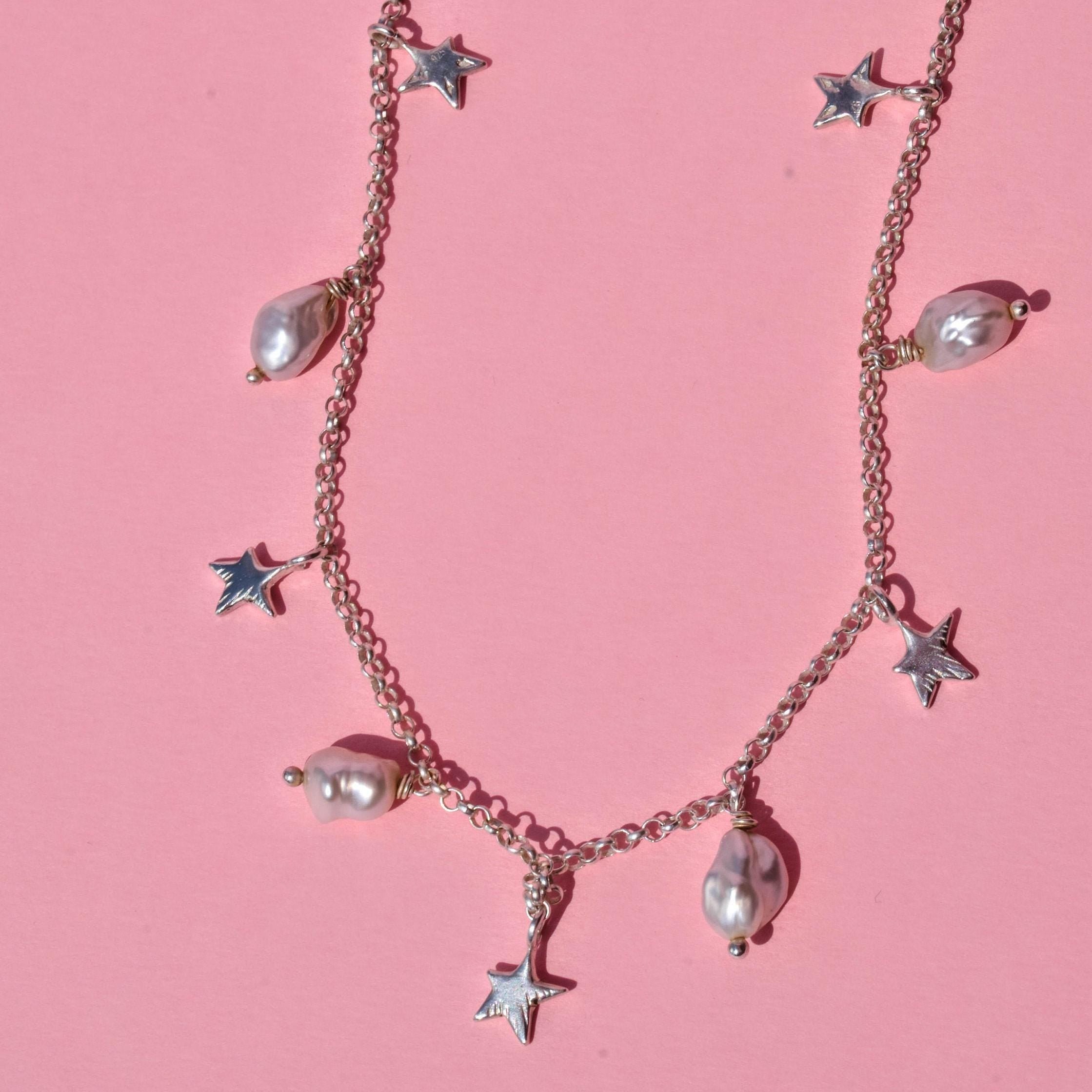A choker necklace with irregular pearl beads and silver stars charms, displayed against a pink background.