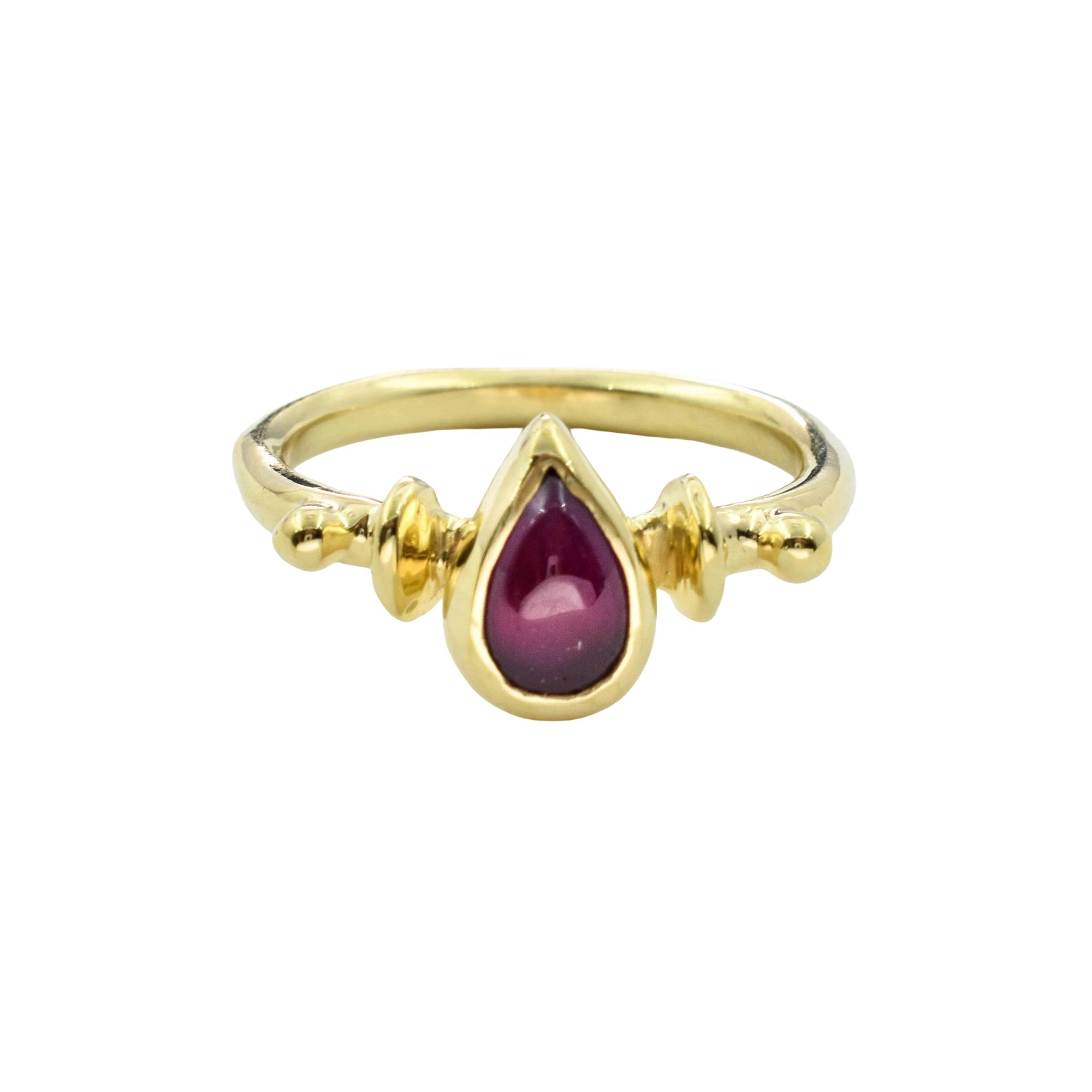 A gold ring featuring a teardrop-shaped dark red gemstone in the center, flanked by small gold bead details on the band, set against a plain white background.