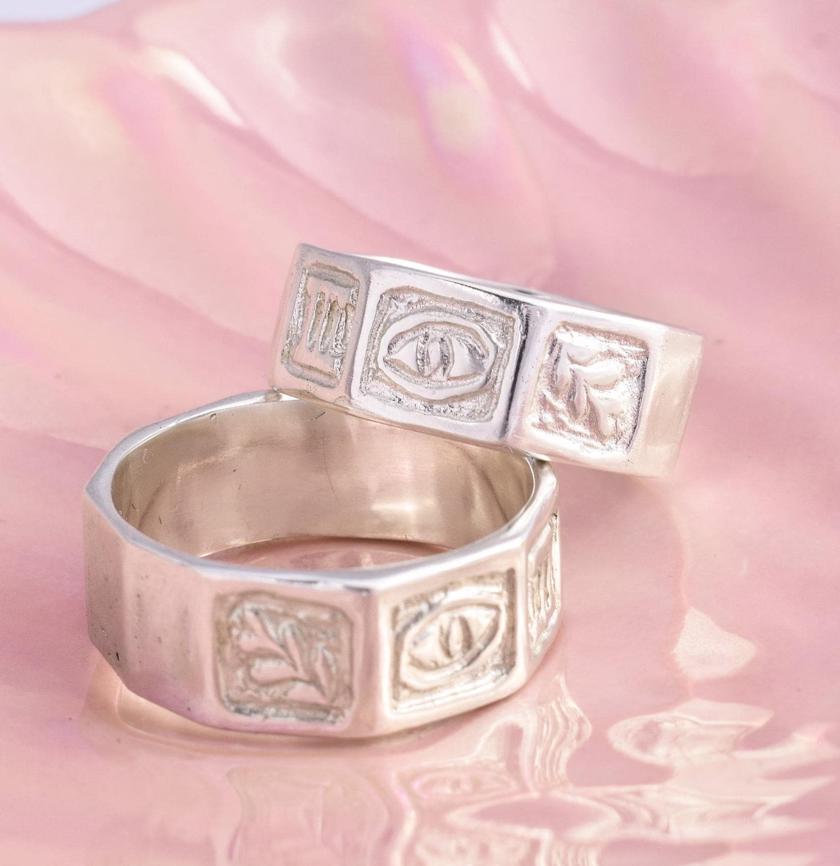 A sterling silver band ring with hand-carved patterns including an evil eye and leaves, displayed on a pink background.