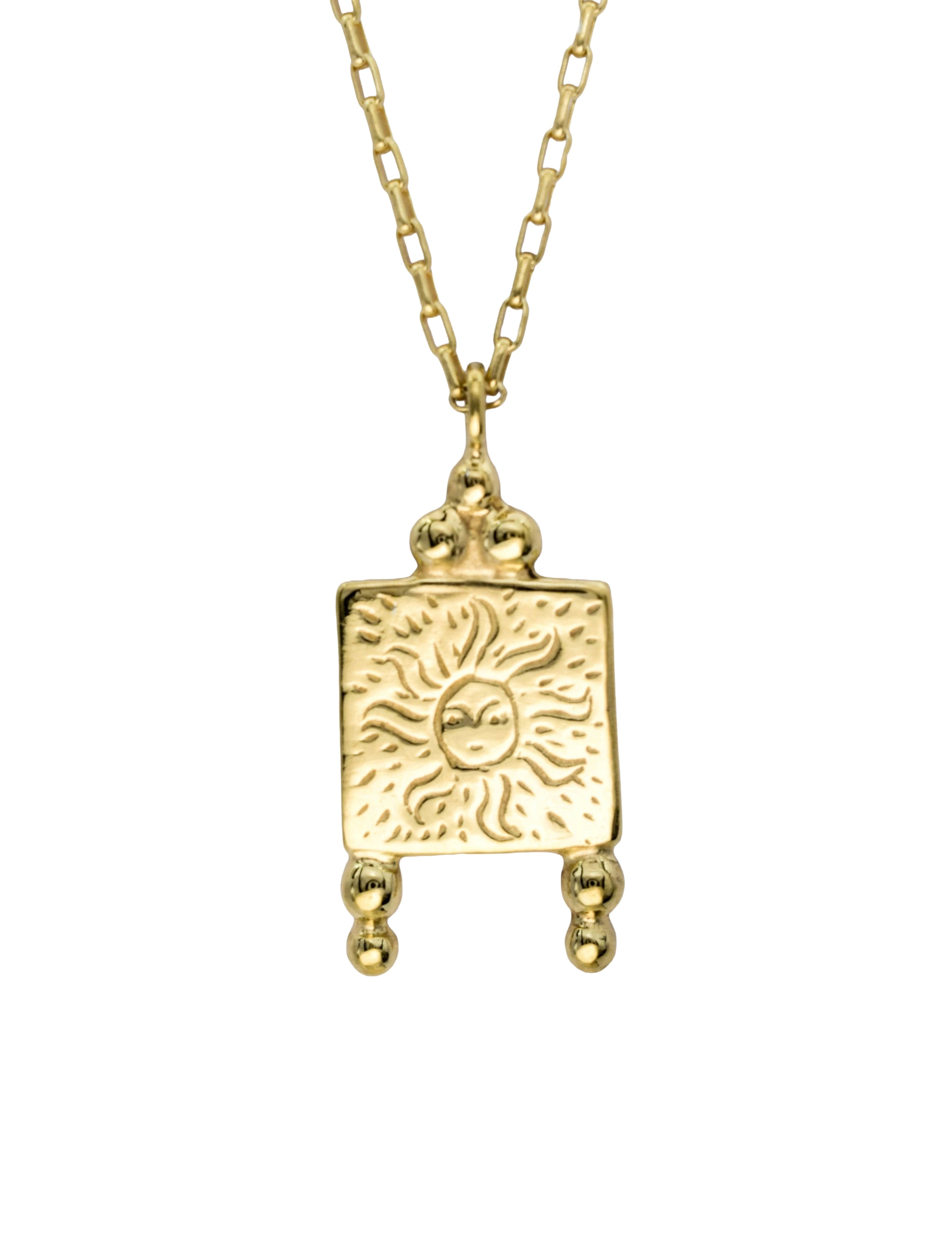 A gold pendant necklace featuring a square charm with an embossed sun design, suspended from a gold chain against a plain white background.