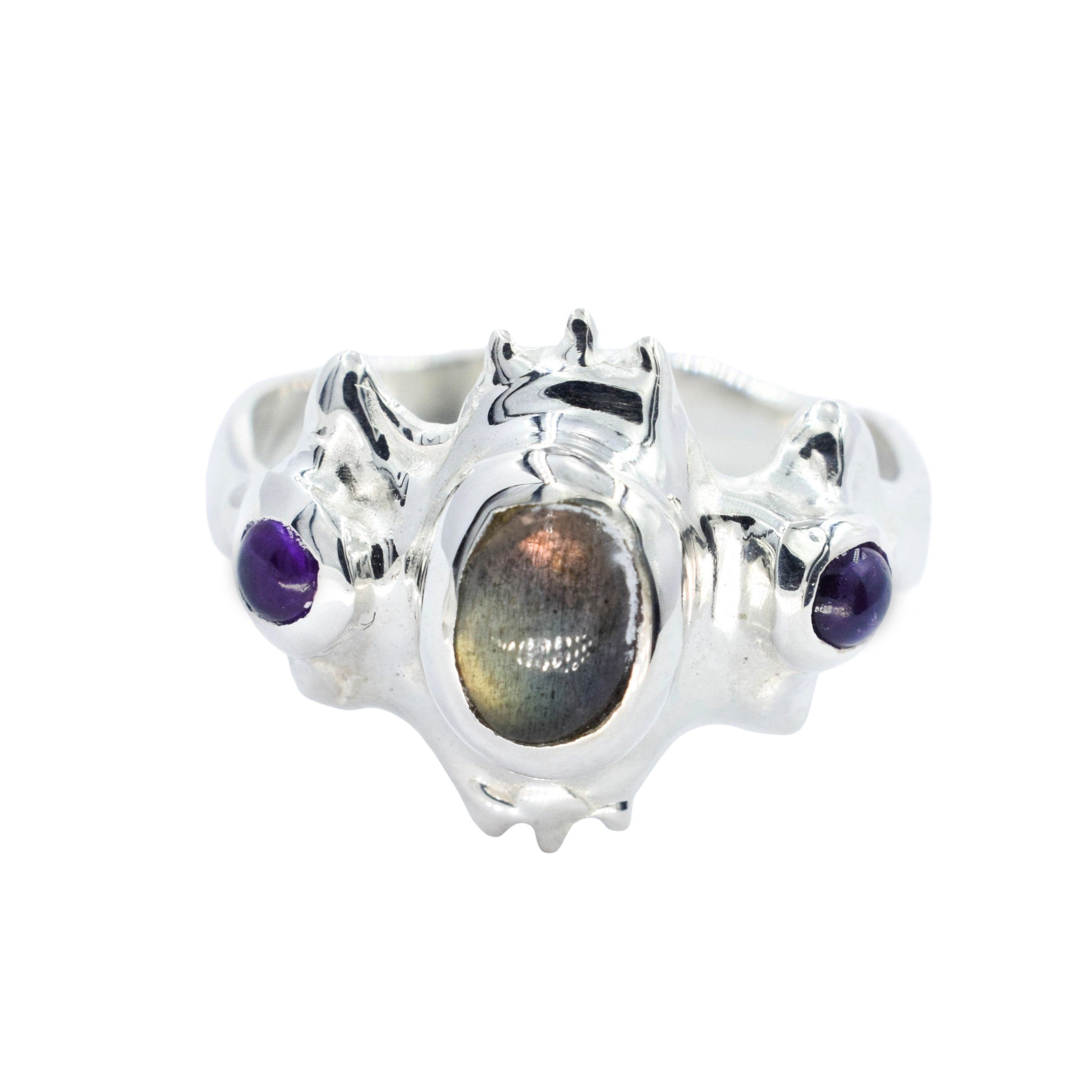 A silver ring featuring a central oval iridescent labradorite stone and two small round purple gemstones on either side, shown on a plain white background.