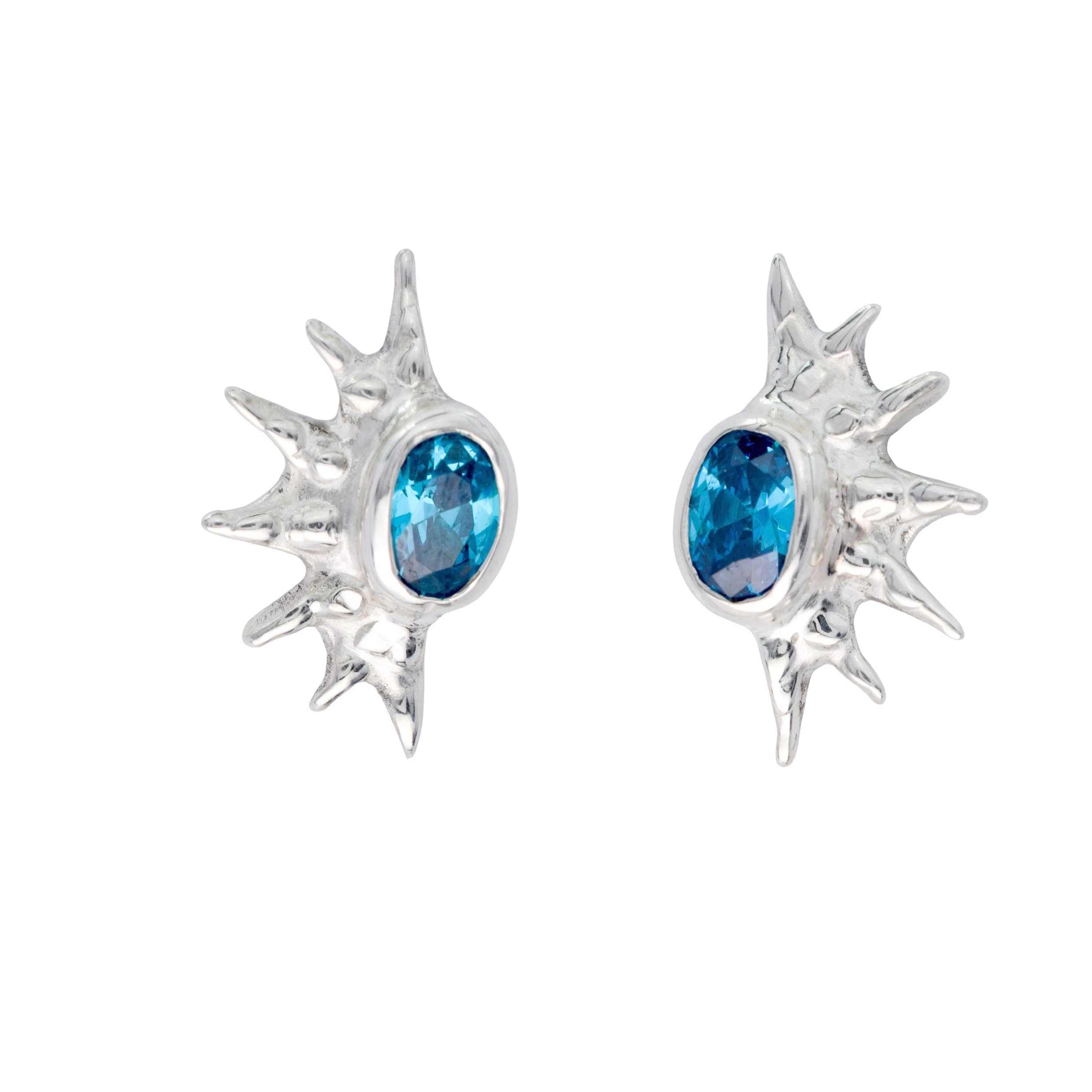 A pair of silver sunburst stud earrings with oval blue gemstones.