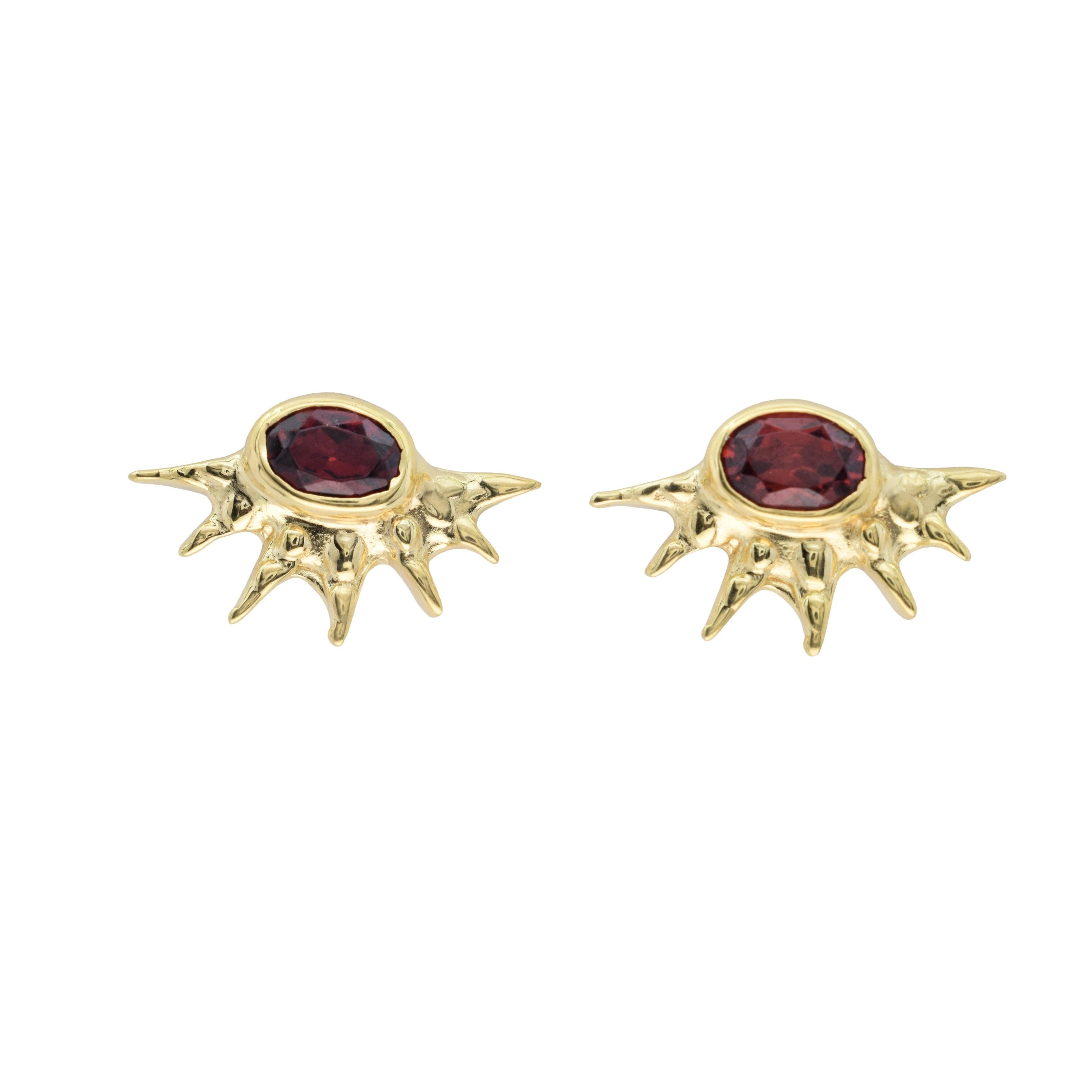 A pair of gold-toned spiky stud earrings with oval dark red gemstones, displayed on a clean white background.