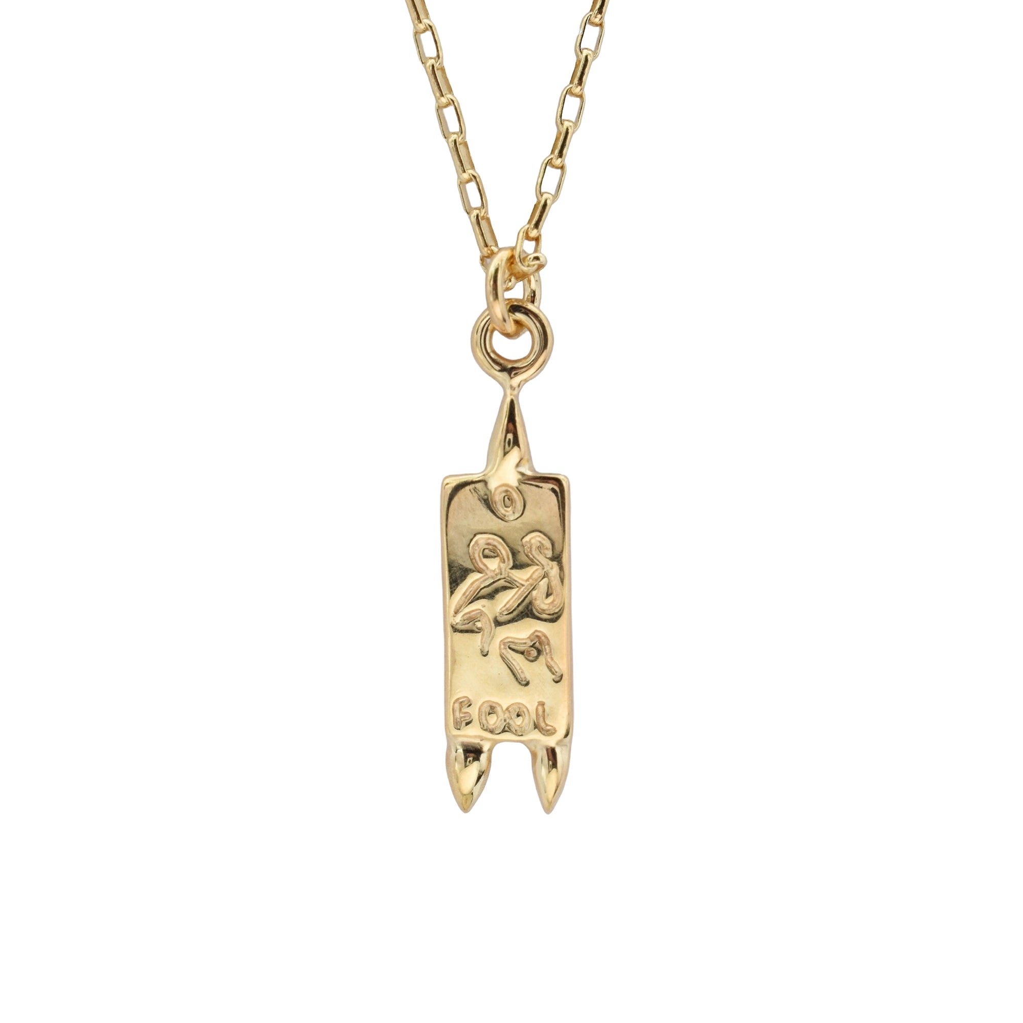 A gold pendant necklace featuring a vertical banner-shaped charm with an engraved figure and the word 'FOOL', suspended from a gold link chain against a plain white background.