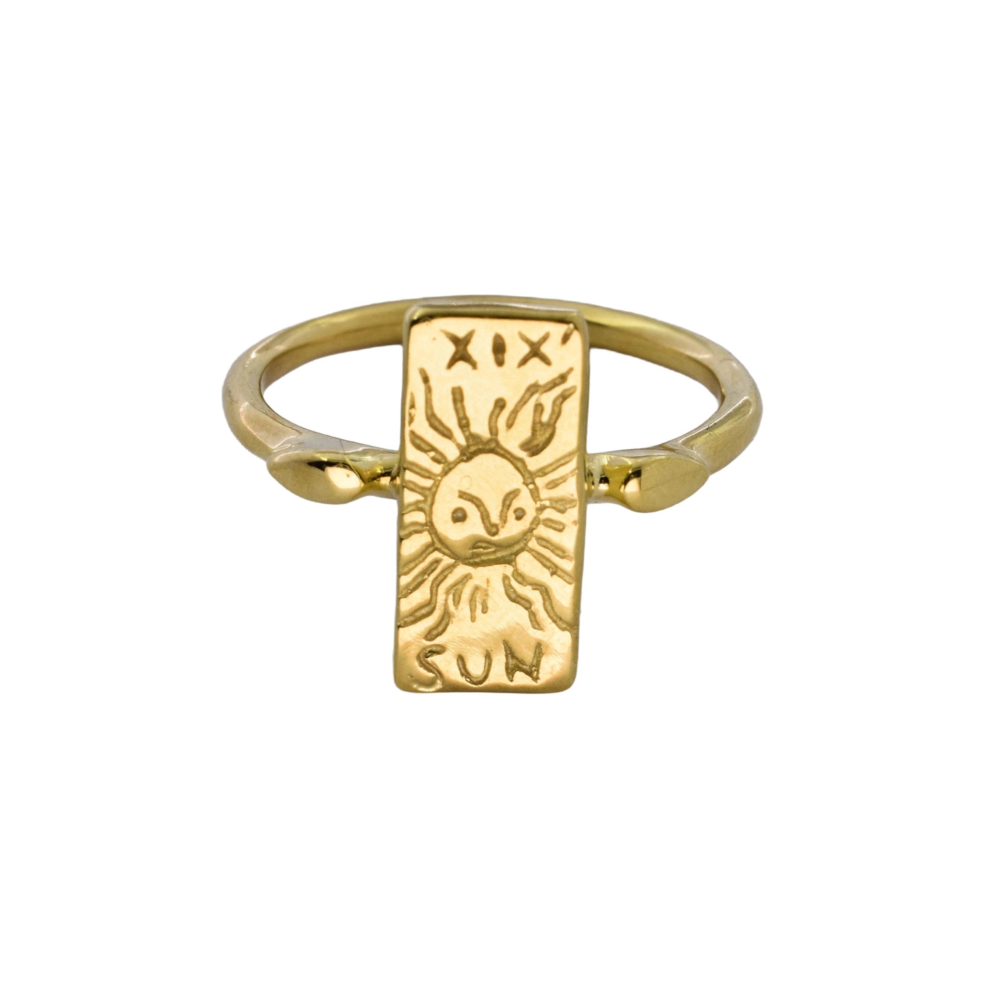 A gold signet ring featuring a rectangular sun face pendant with carved symbols, shown on a plain white background.