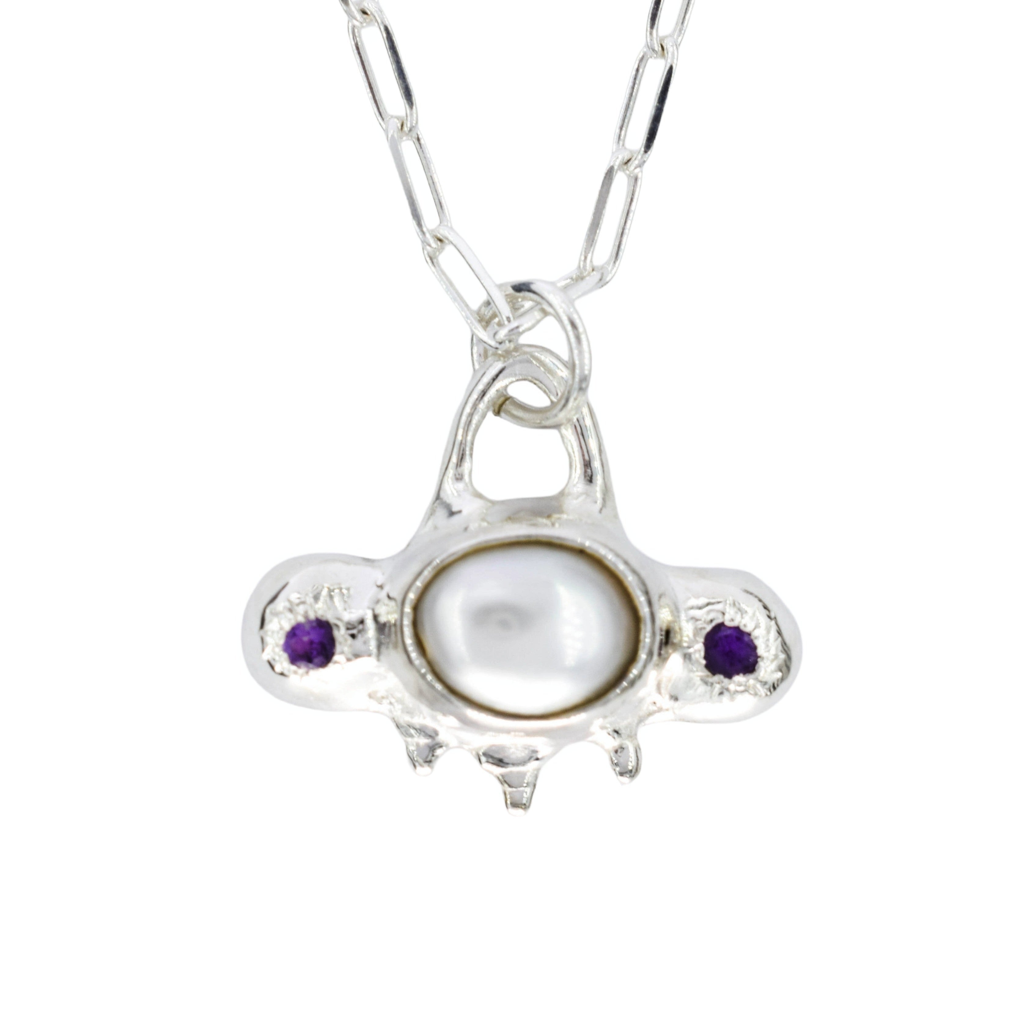 A silver pendant necklace featuring a central white pearl surrounded by two small purple gemstones, suspended from a silver link chain on a white background.