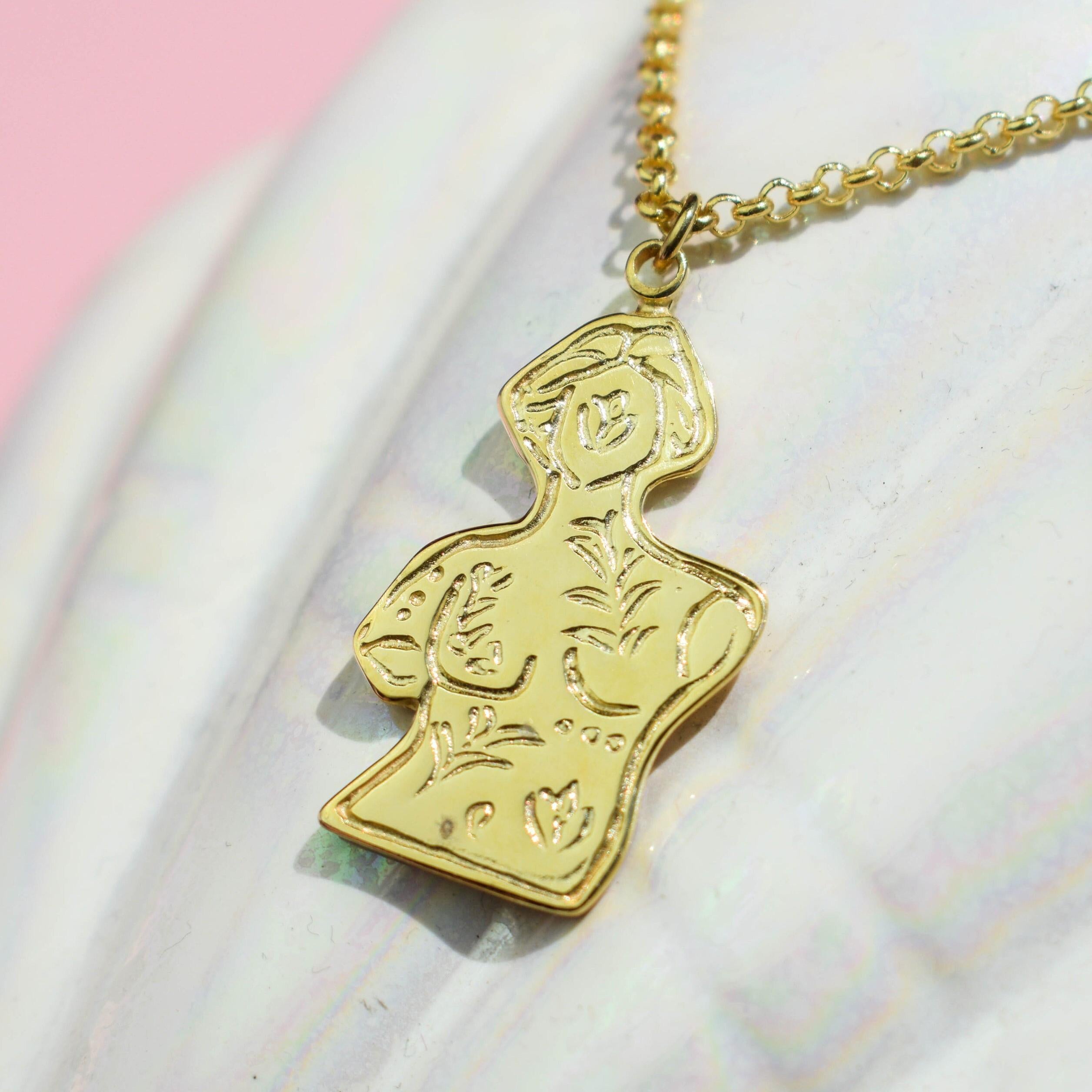 A gold-colored necklace featuring a pendant with leaf and flower patterns on a marble surface.