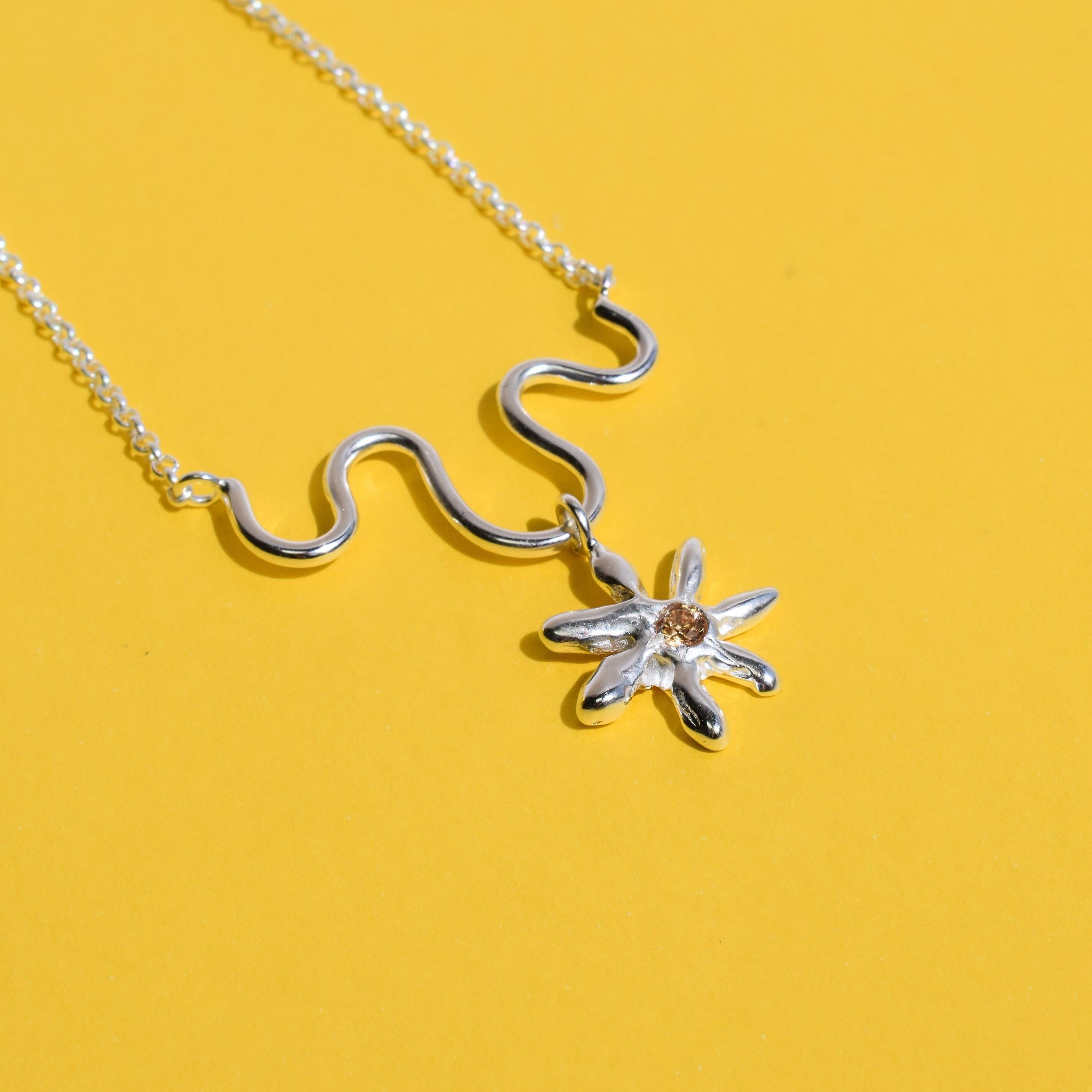 A silver necklace with a champagne cubic zirconia daisy flower pendant on a yellow background.