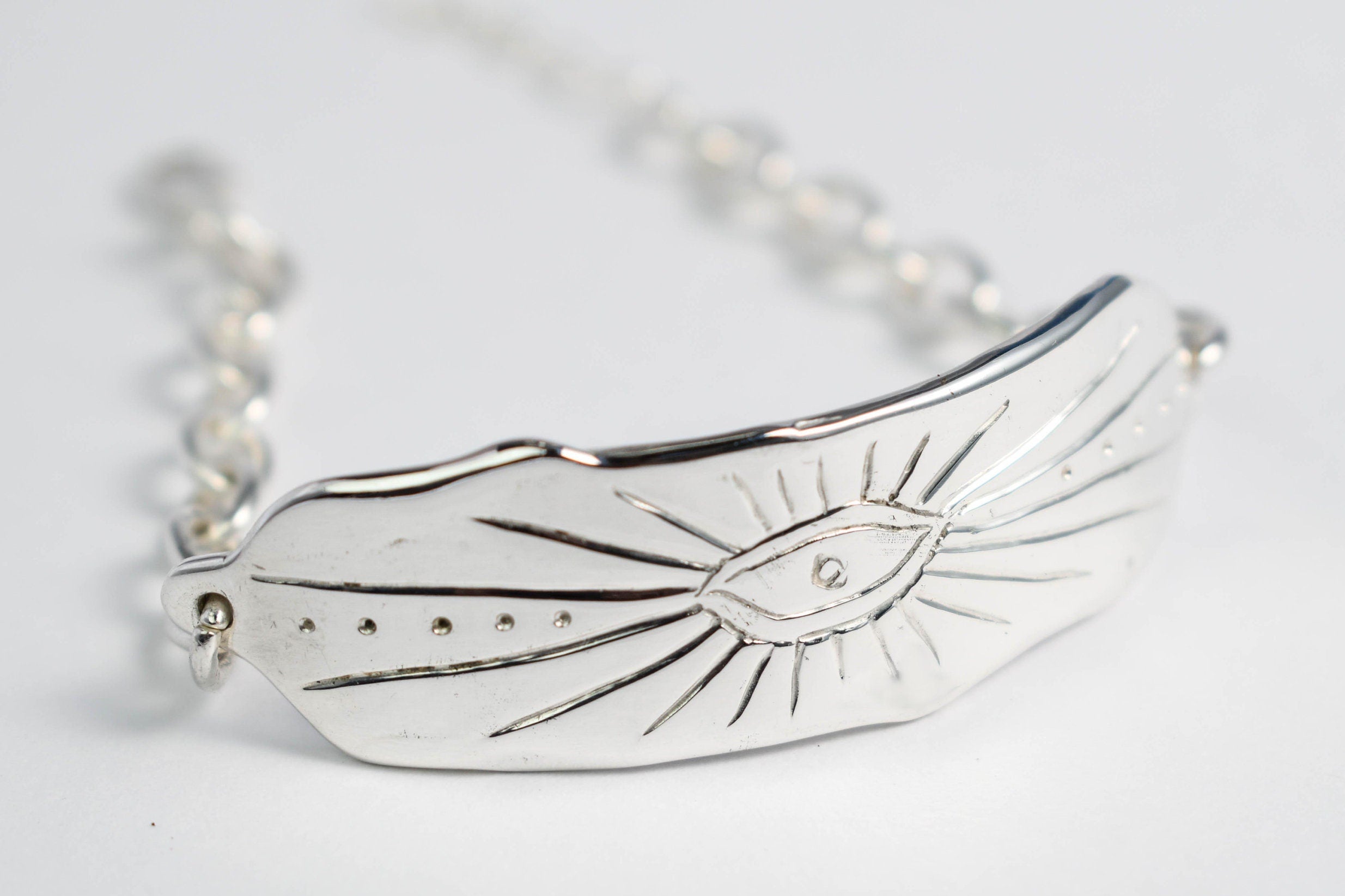 A silver chain bracelet with a tag featuring a stylized eye design, known as an evil eye bracelet.