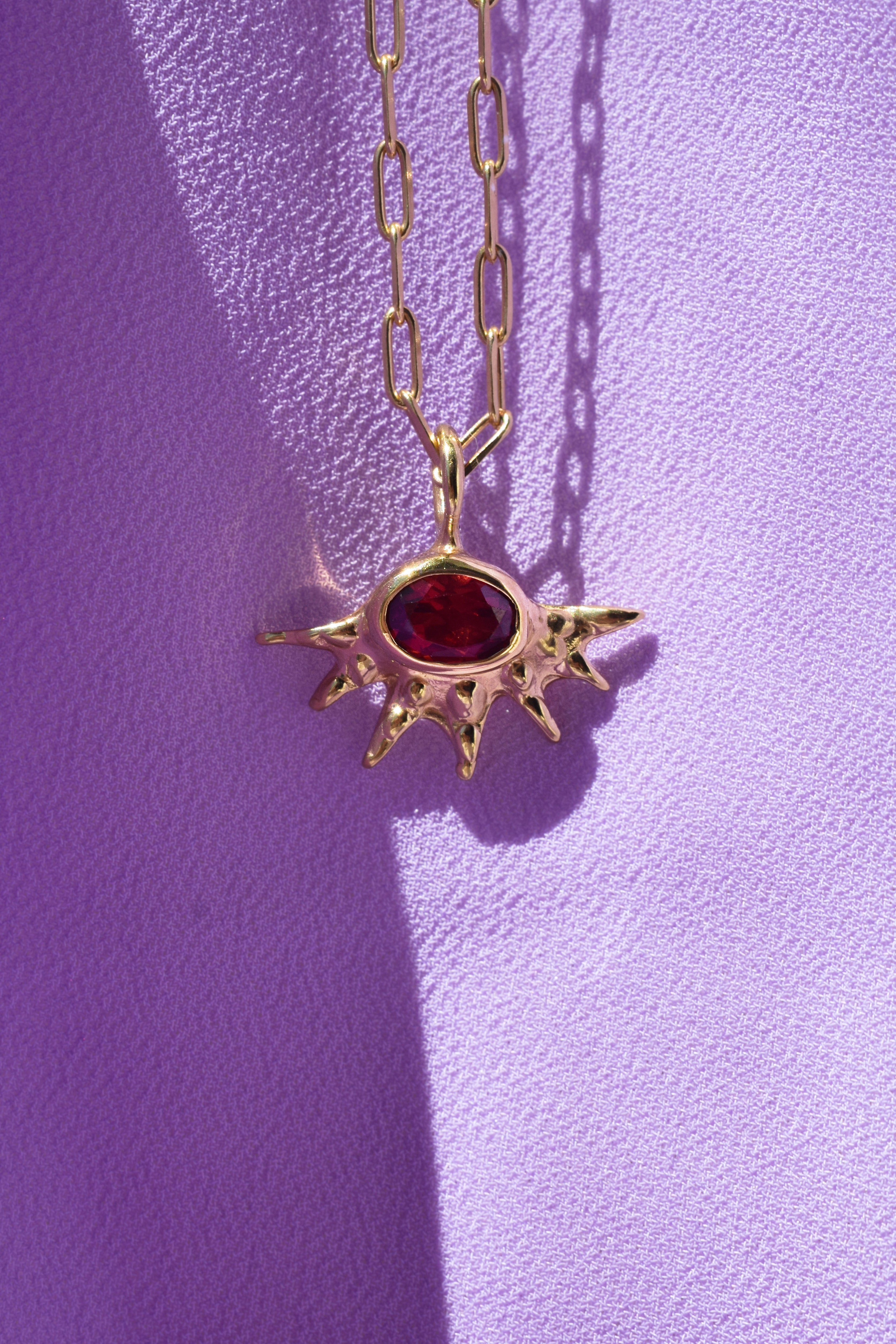 A radiant pendant on a paperclip chain, featuring a deep red garnet at the center of an asymmetrical, spiked gold setting. Bold and edgier than a traditional sunburst, it's easy to wear solo or layered.