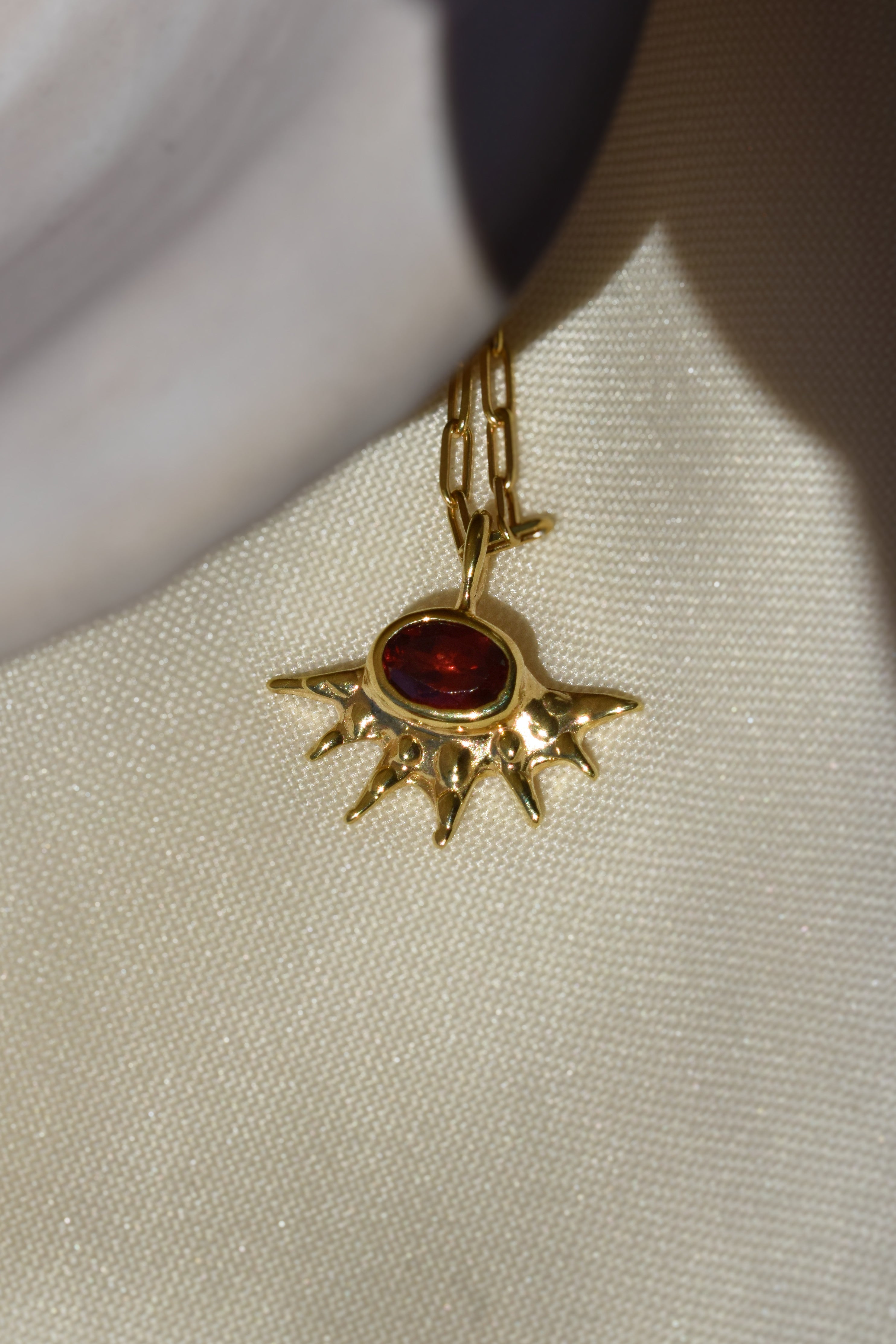 A radiant pendant on a paperclip chain, featuring a deep red garnet at the center of an asymmetrical, spiked gold setting. Bold and edgier than a traditional sunburst, it's easy to wear solo or layered.