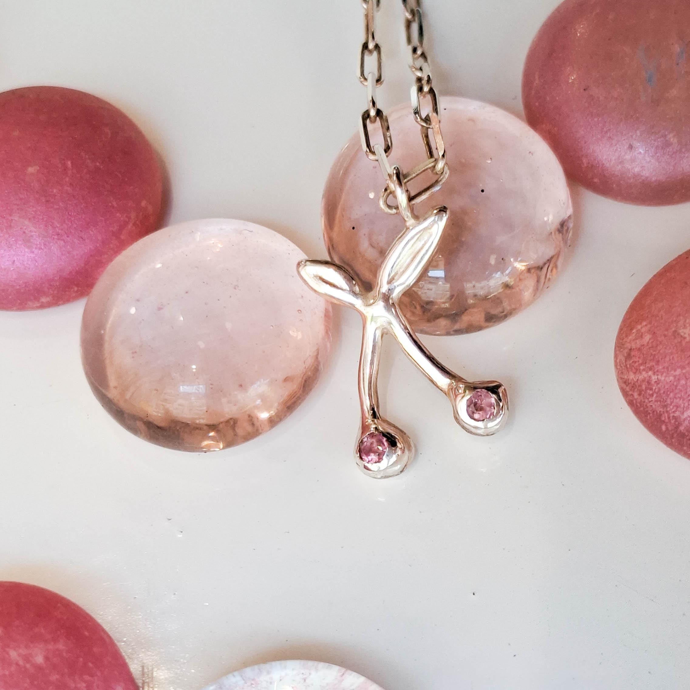 Gold necklace with a leaf-shaped pendant featuring pink gemstones on a white background.