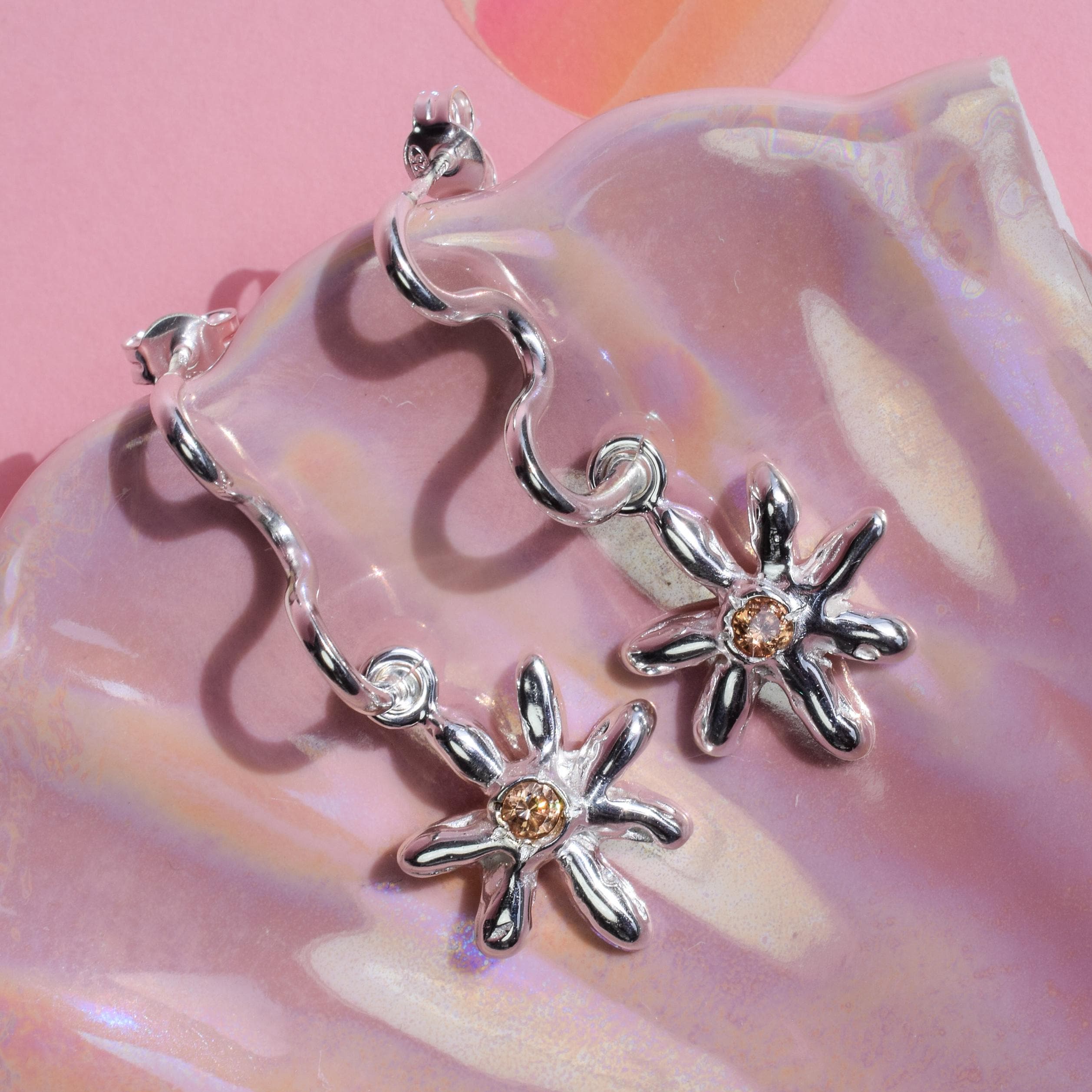A pair of daisy-shaped drop earrings with champagne zircon crystals, displayed on a reflective surface.