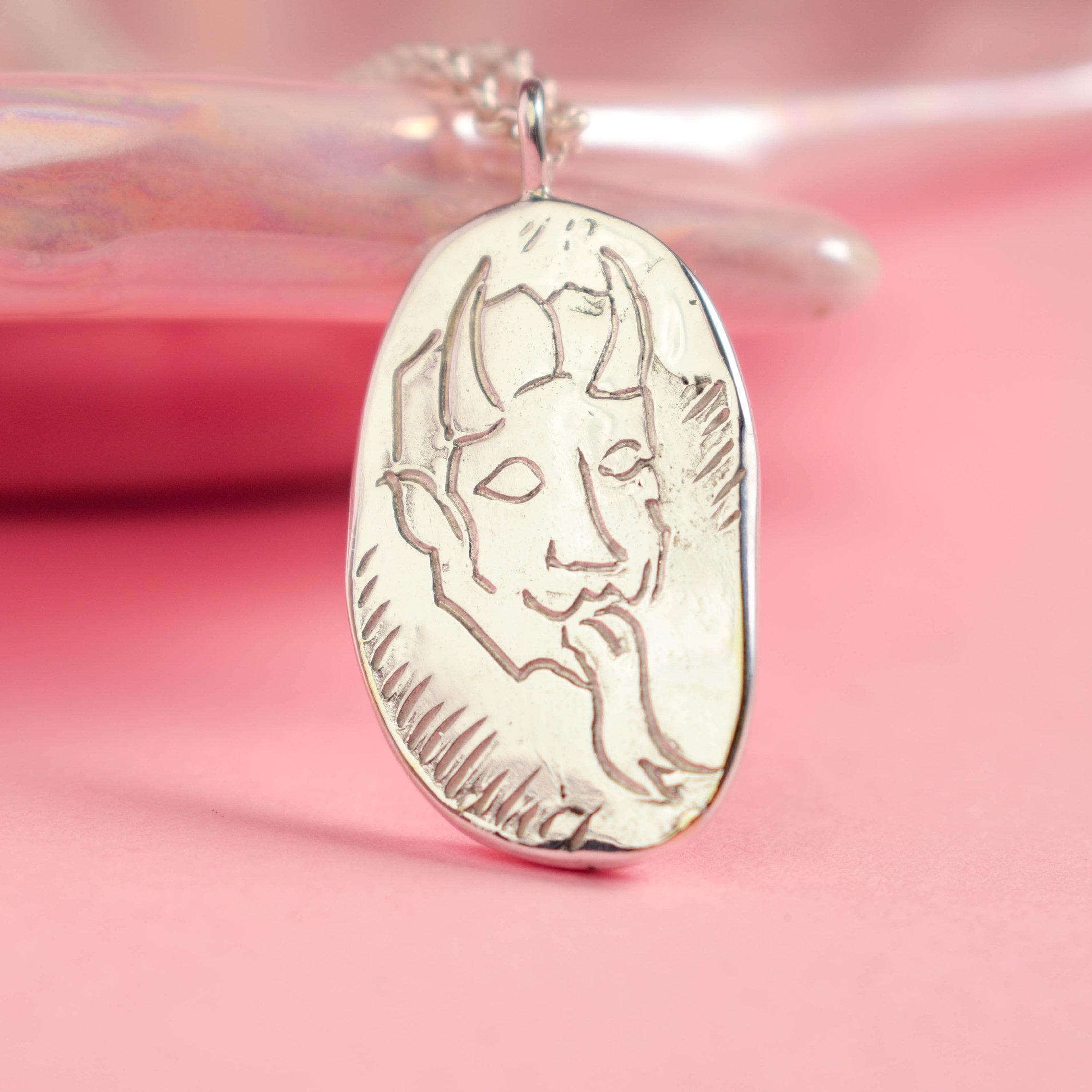 A silver pendant necklace featuring a hand-carved design of a devil's face with horns.