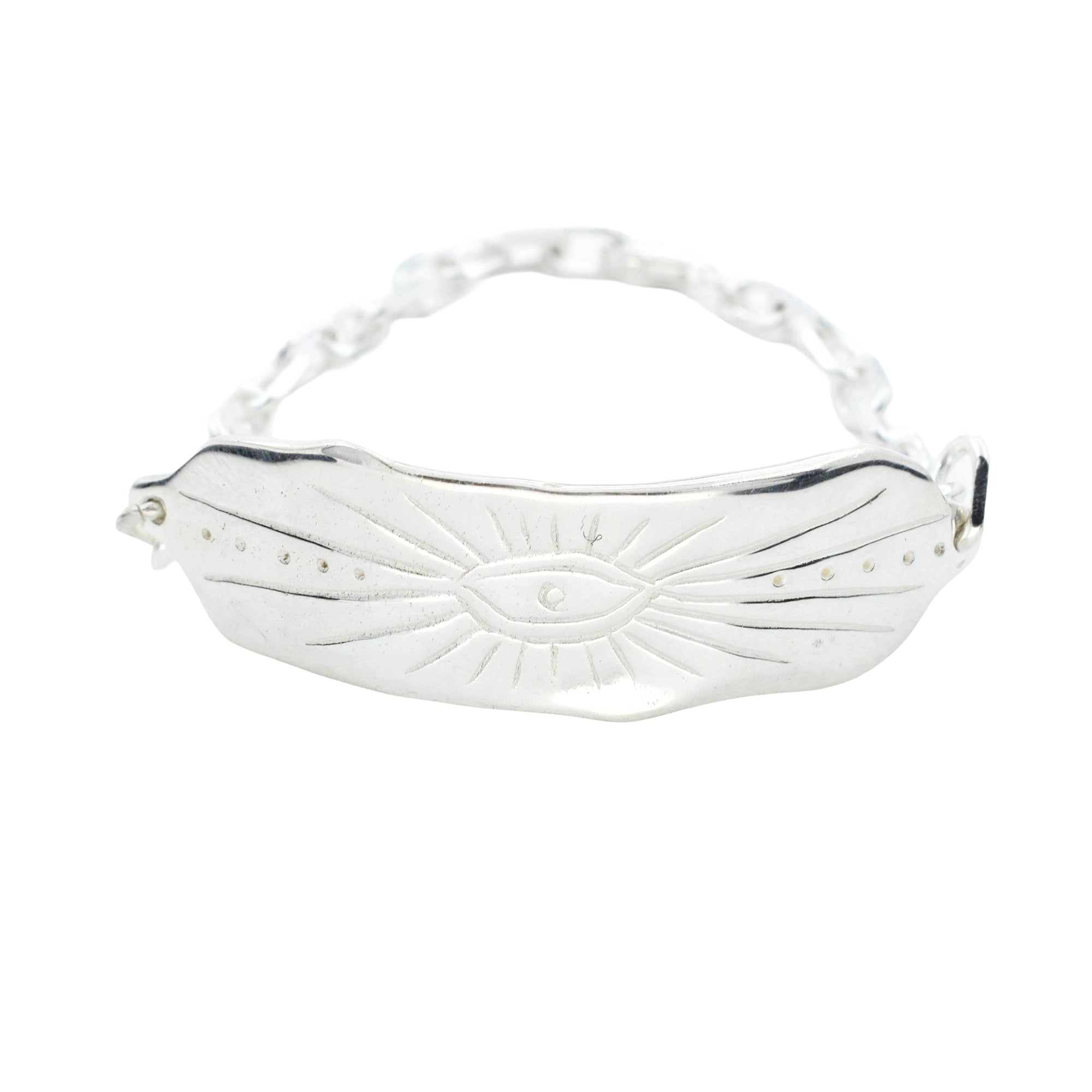 A silver-toned metal bracelet featuring a curved bar engraved with a central eye motif and small dots, connected by a delicate chain on a plain white background.