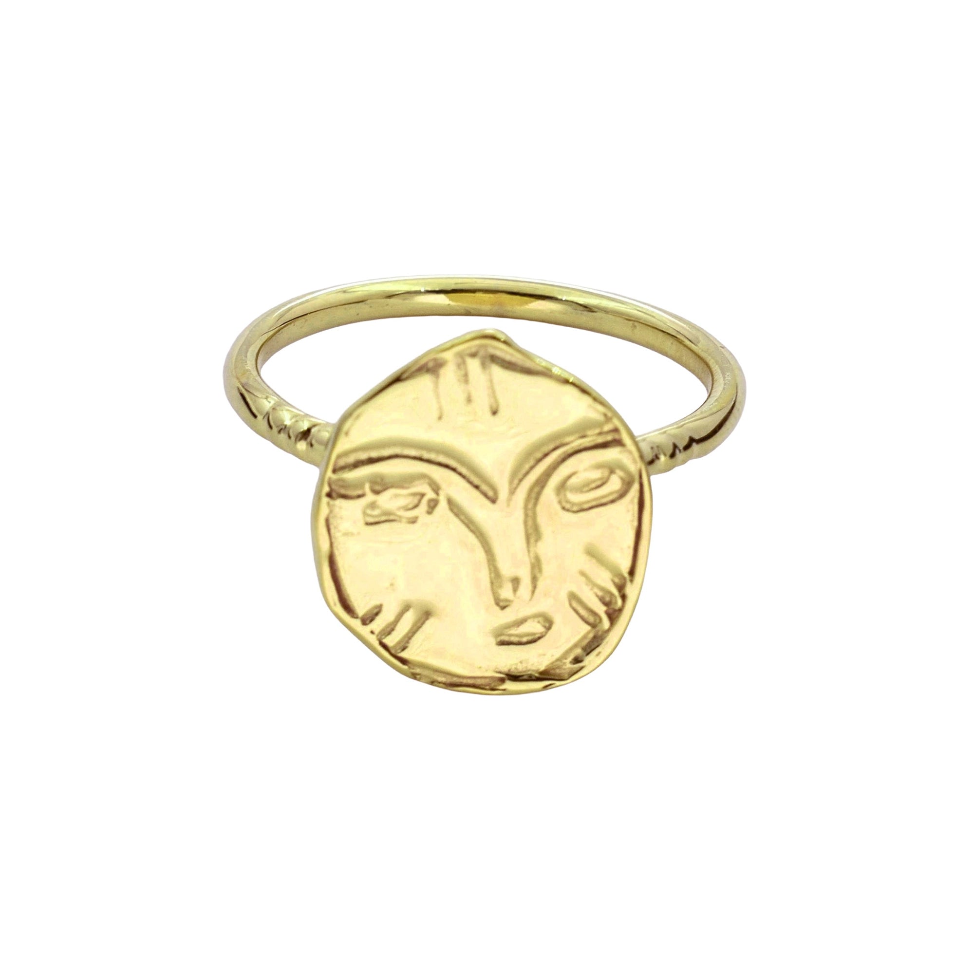 A gold ring featuring a textured, hand-drawn style oval face pendant with stylized eyes and a nose, set against a plain white background.