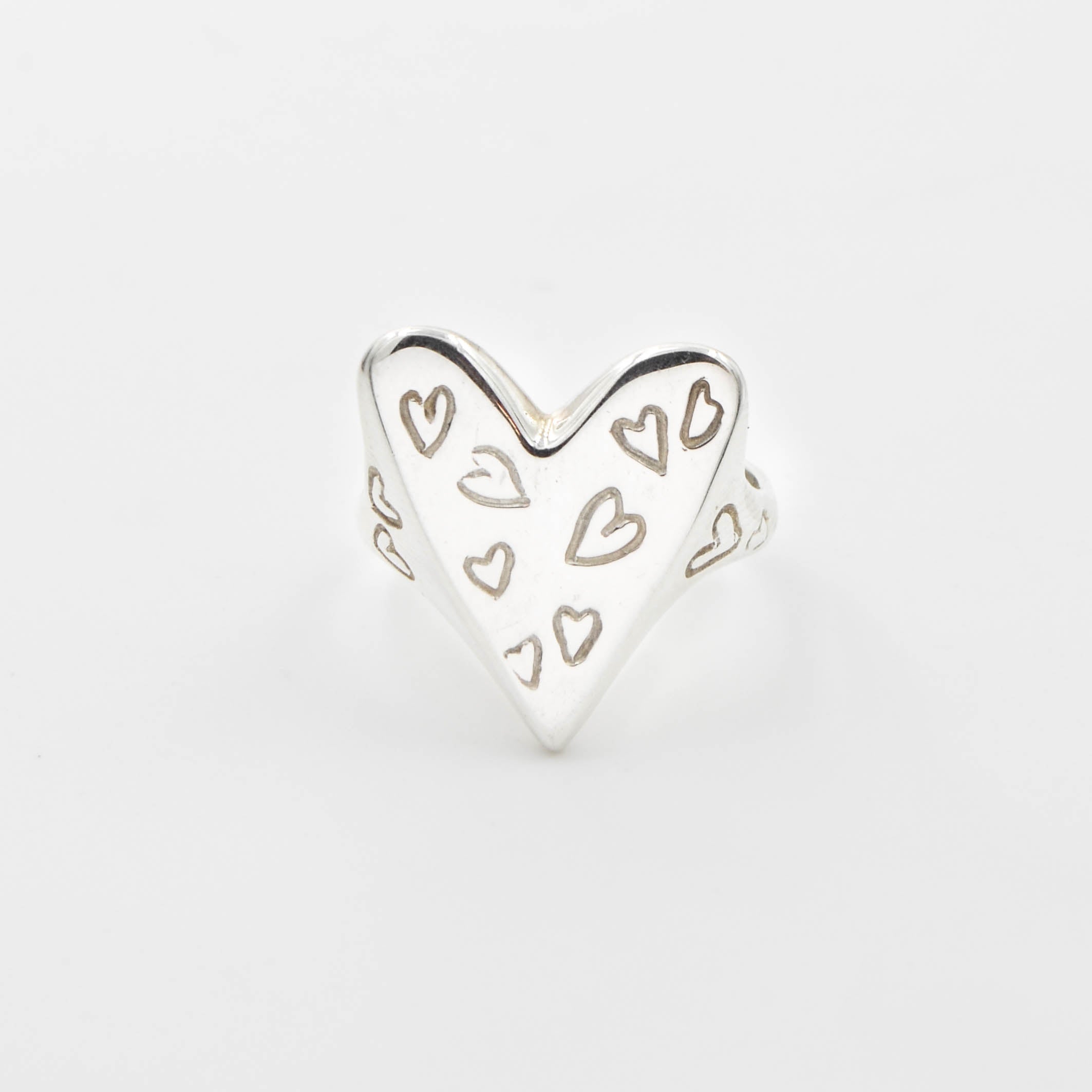 Heart-shaped silver ring with cut-out heart designs on a light gray background