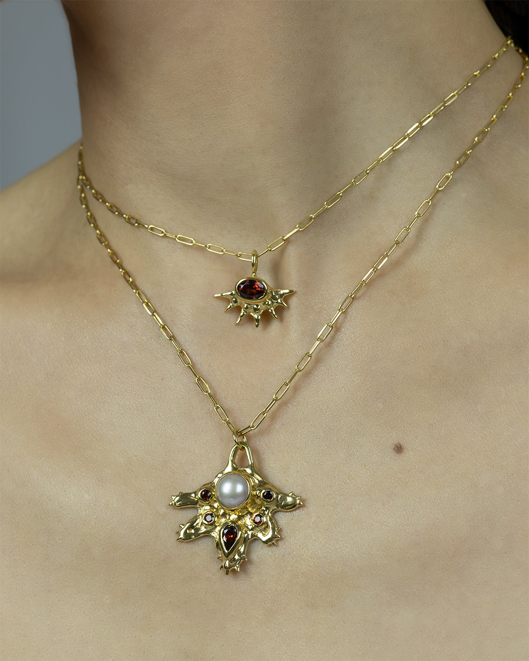 A radiant pendant on a paperclip chain, featuring a deep red garnet at the center of an asymmetrical, spiked gold setting. Bold and edgier than a traditional sunburst, it's easy to wear solo or layered.