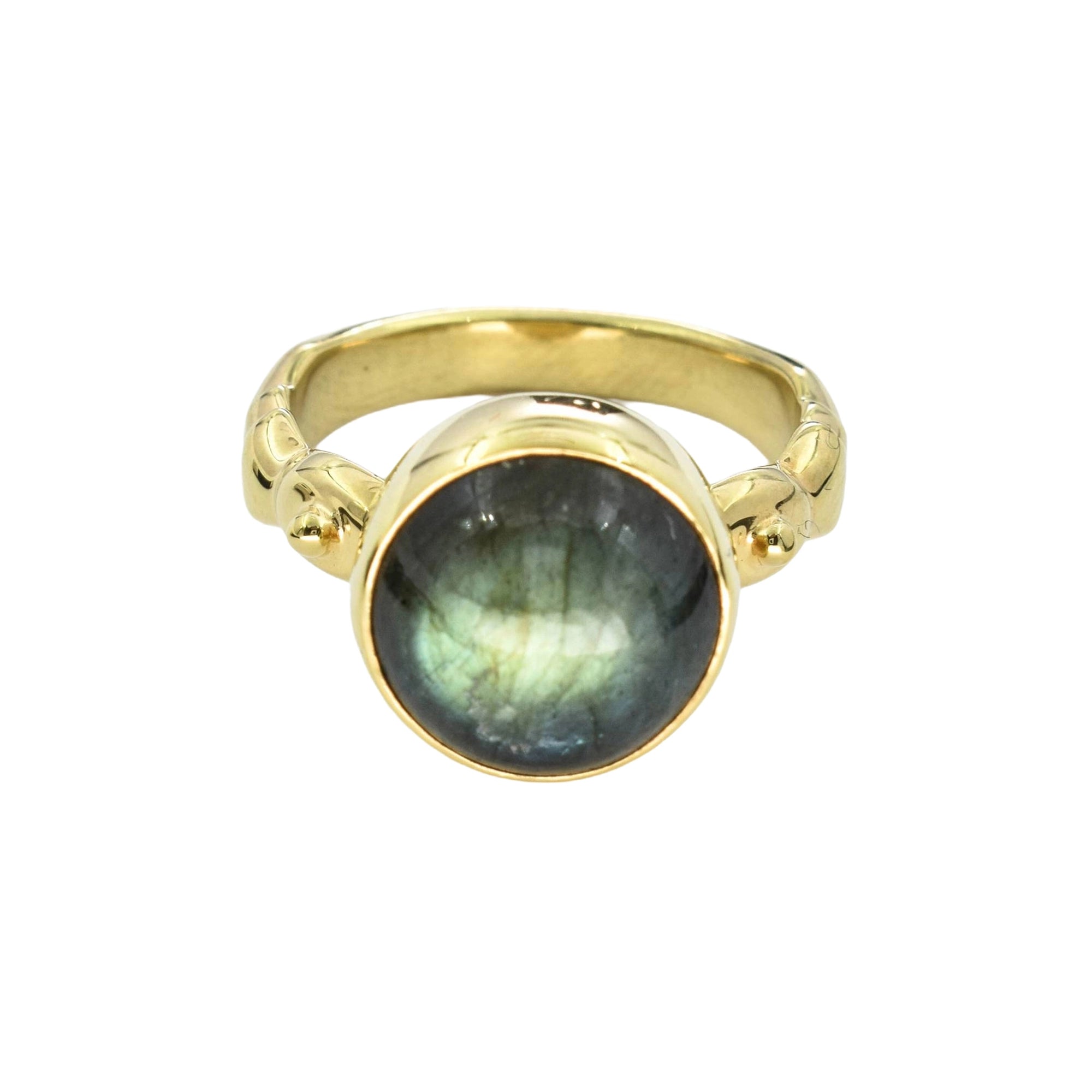 A gold ring featuring a large oval cabochon gemstone with a greenish-gray labradorite flash, set against a plain white background.