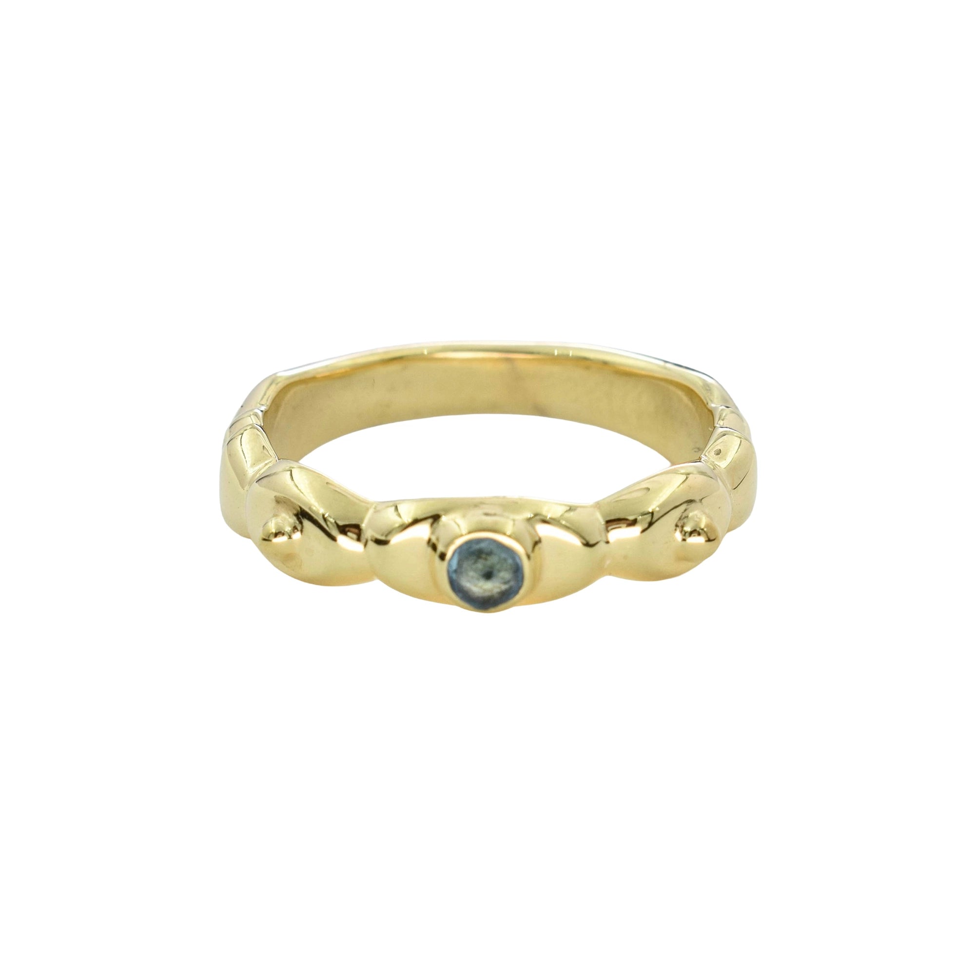 A gold ring with a textured, organic-shaped band and a small round blue gemstone in the center, shown on a plain white background.