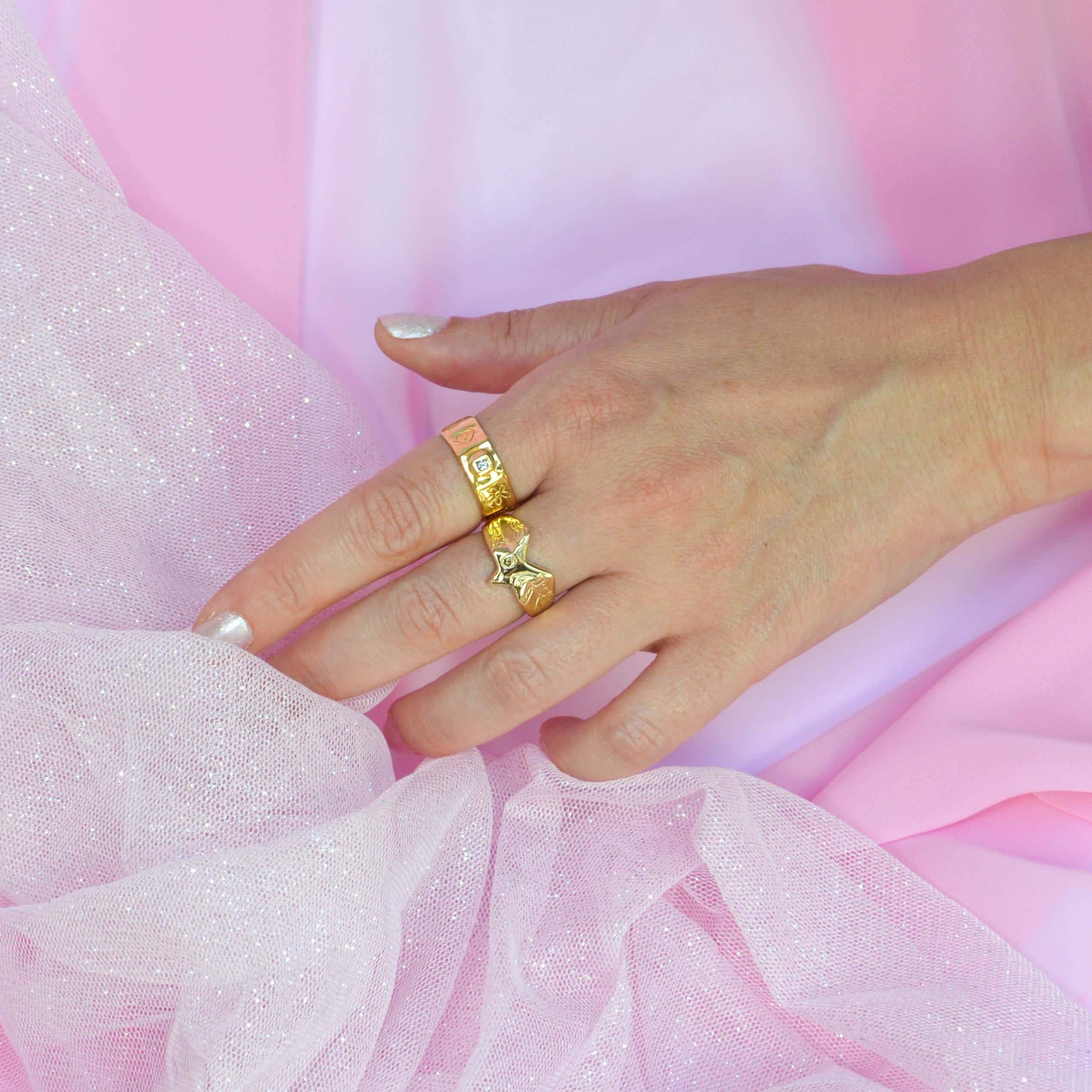 Hand wearing gold rings on a pink fabric background