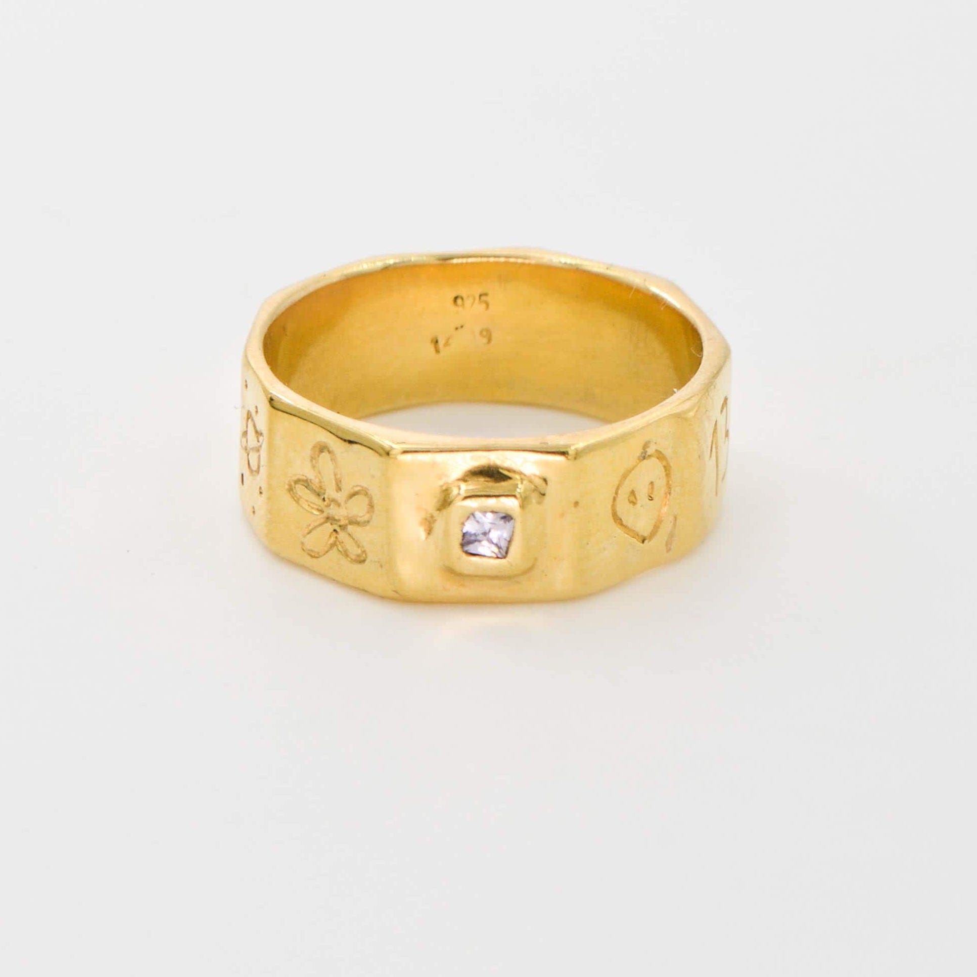 Gold ring with engraved designs on a white background