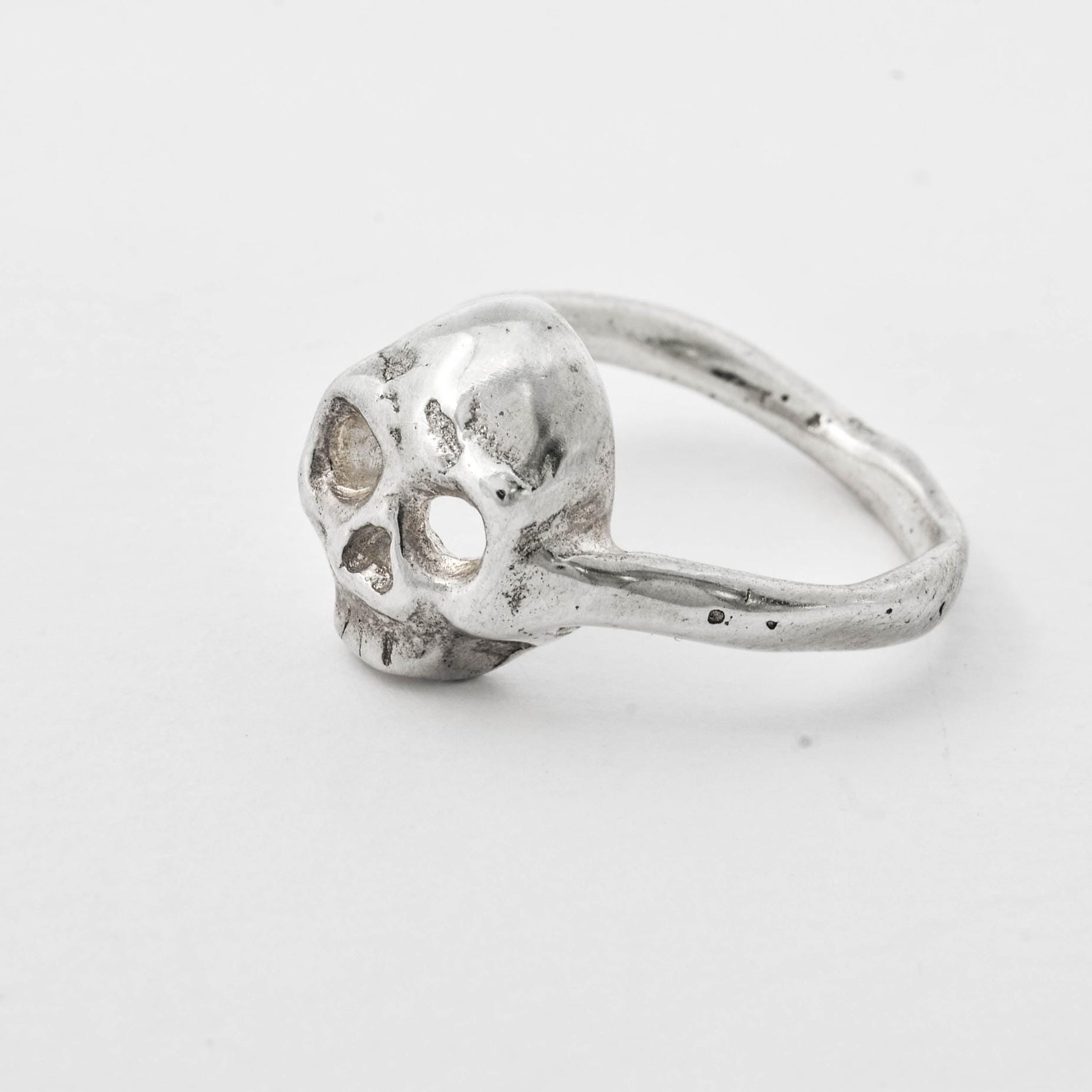 A handcrafted silver skull ring with a textured surface on a white background.