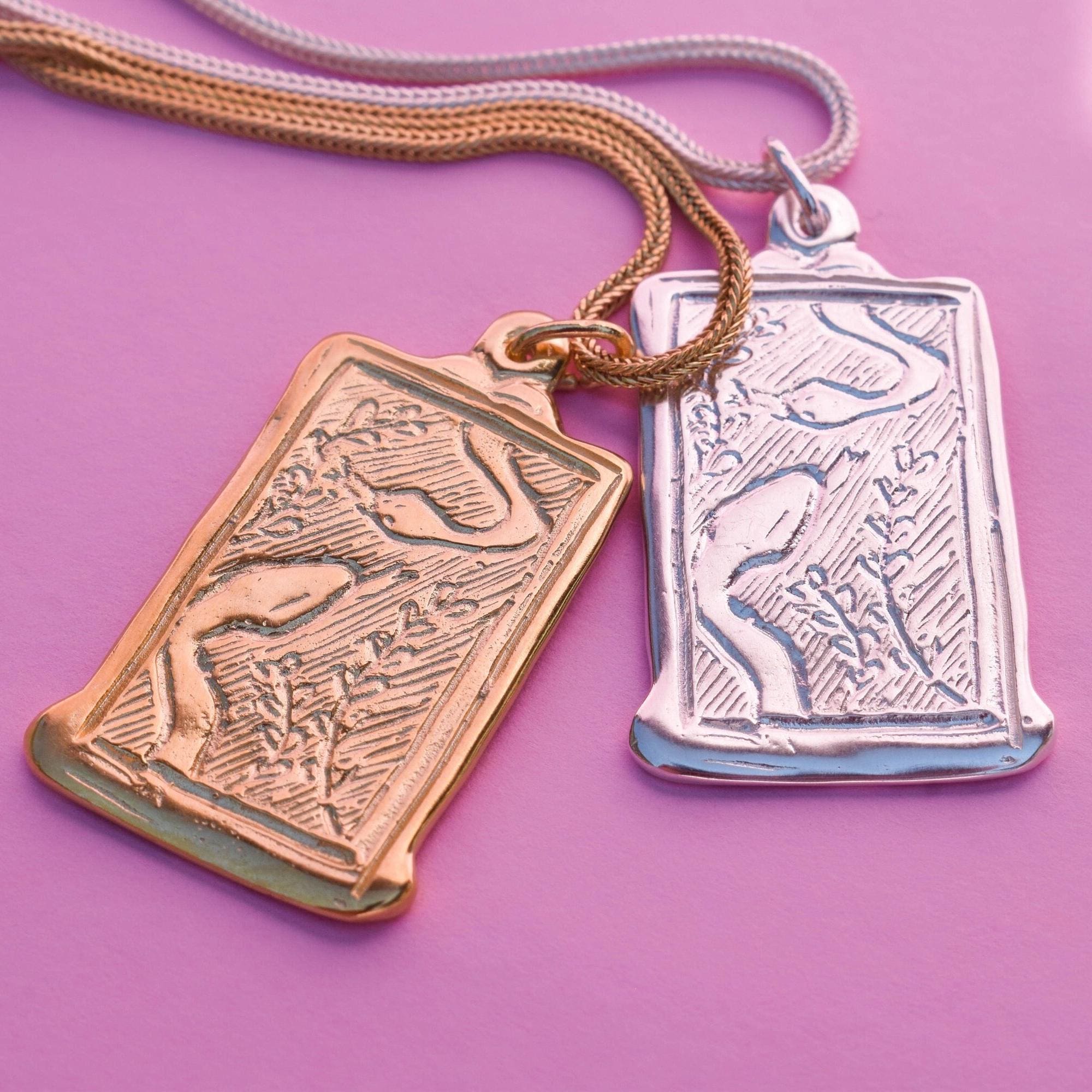 Two rectangular snake pendant necklaces, one with a gold-tone and the other with a silver-tone, both featuring intricate carvings.