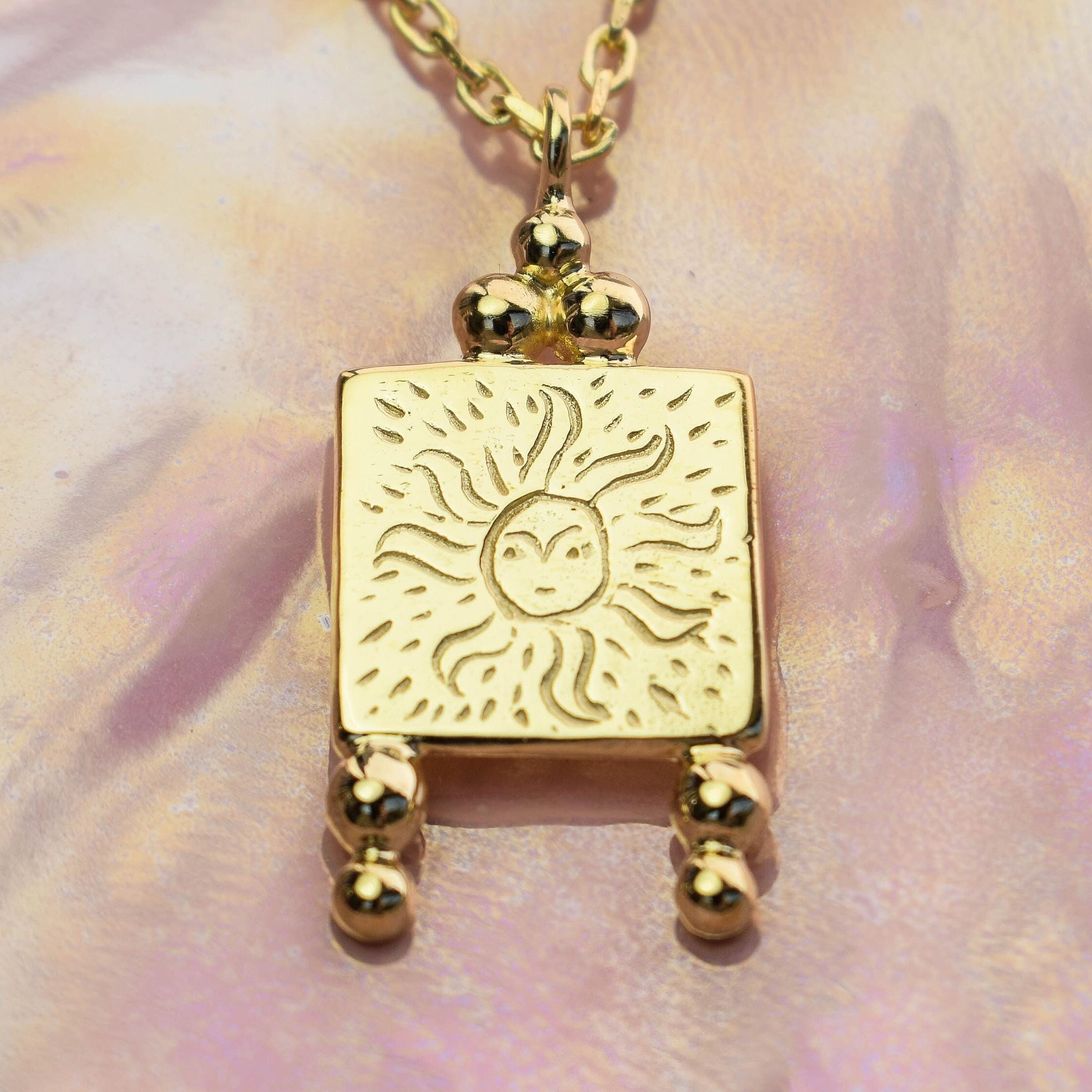 A gold-colored vintage style sun necklace pendant with alchemical engravings, suspended from a chain.