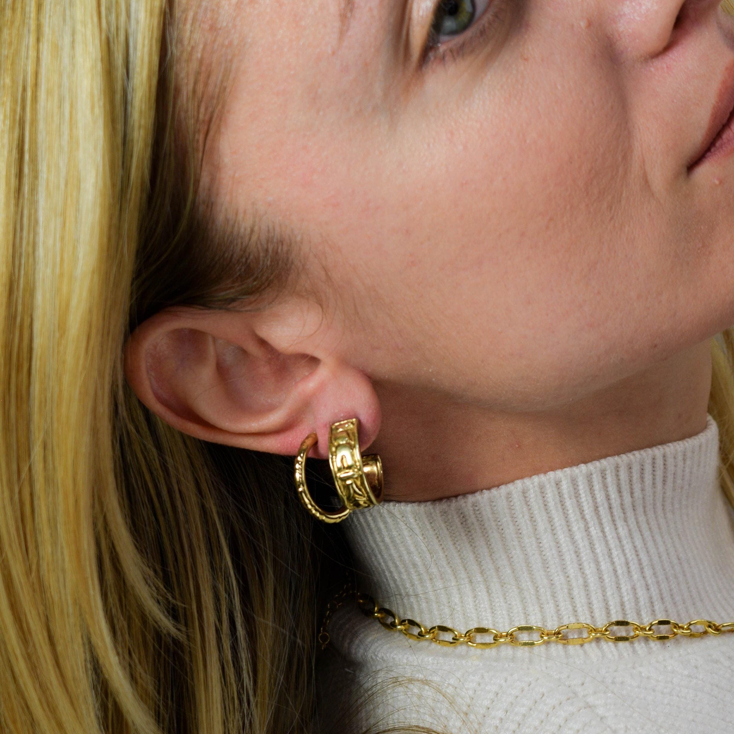 A close-up image of a person wearing thick, wide gold hoop earrings.